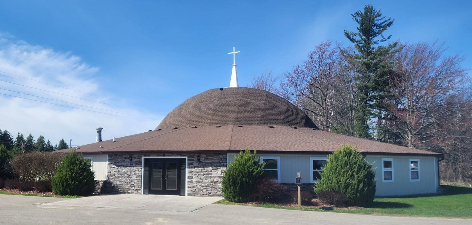 The dome sanctuary of Houghton Lake Baptist Church, crowned with a cross against a blue sky